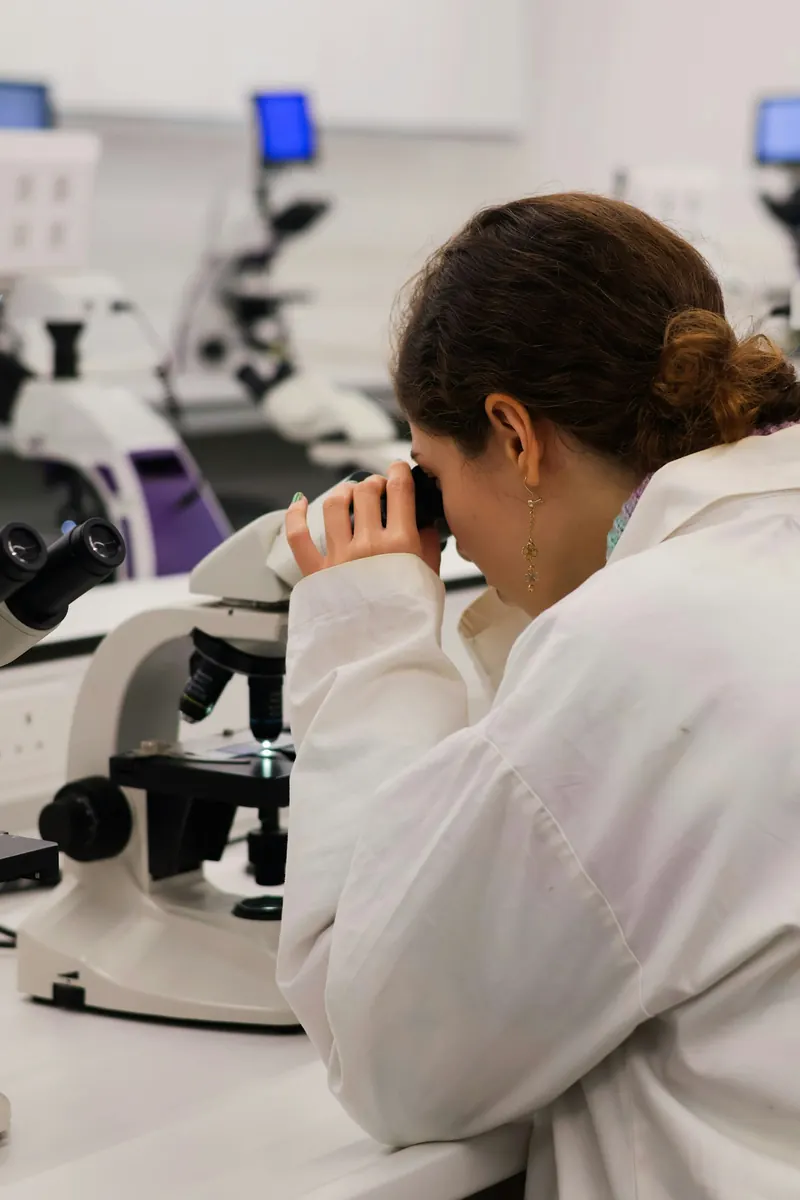 A researcher in a lab coat looks through a microscope in a university laboratory